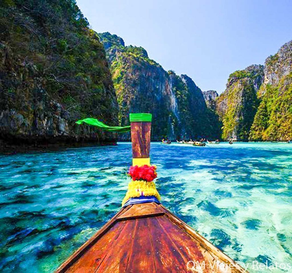 Barca tradicional navegando por aguas turquesas entre acantilados en Tailandia, un paisaje paradisíaco entre las razones para visitar Tailandia.