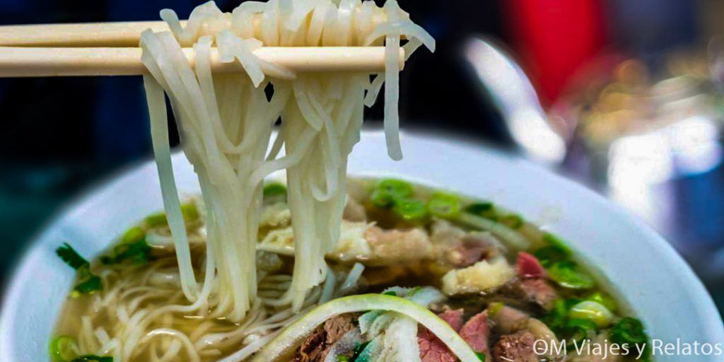 Pho vietnamita con fideos levantados con palillos, plato típico callejero: consejos para viajar a Vietnam por libre y qué comer.