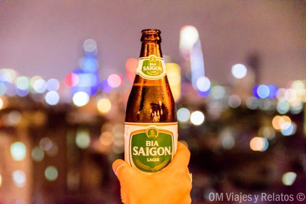 Botella de Bia Saigon con el skyline nocturno al fondo en Nguyen Walking Street, una experiencia urbana que ver en Ho Chi Minh en 1 dia.
