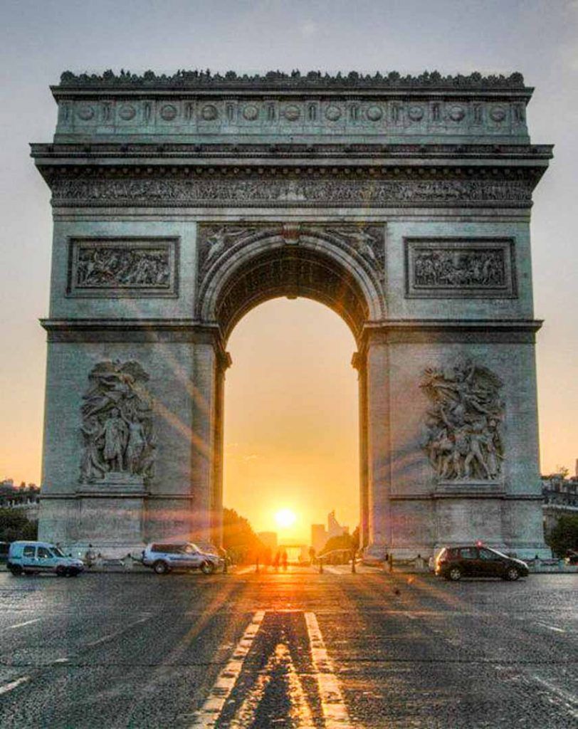 Arco del Triunfo al atardecer con el sol alineado en el centro, una imagen clásica de los monumentos de Paris.