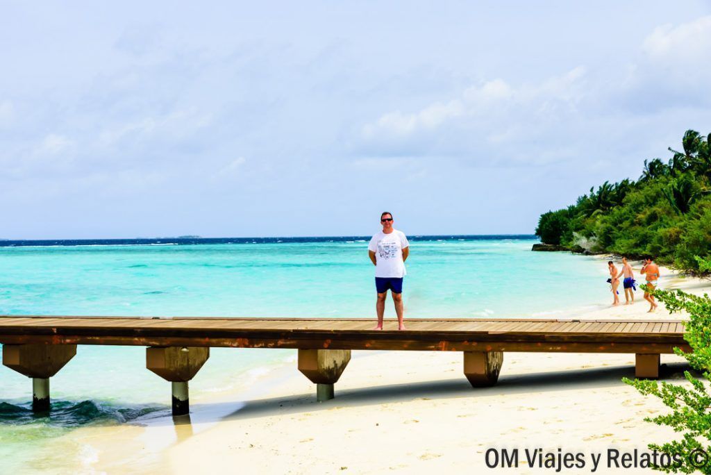 Foto de JC sobre una pasarela de madera frente a una playa de aguas turquesas, una imagen perfecta para inspirarse al viajar a Maldivas por libre.