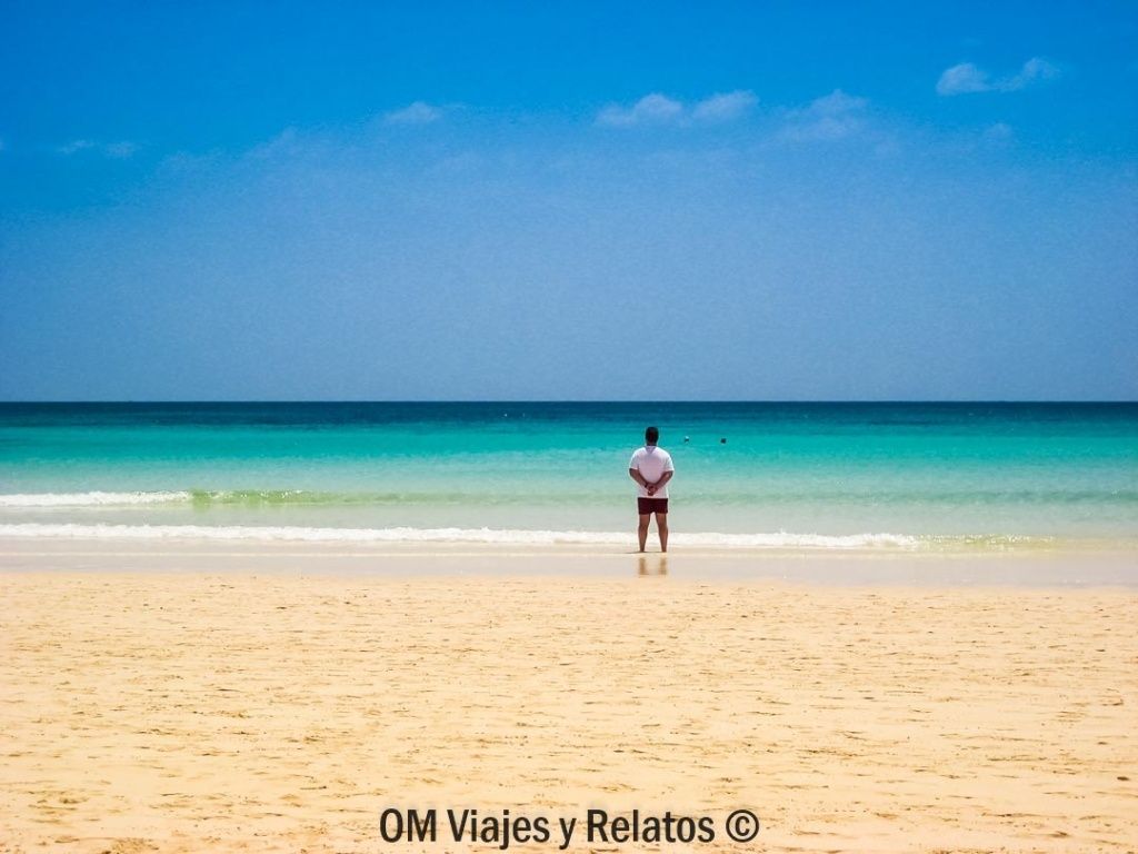 JC contemplando una playa de arena blanca y aguas turquesas en Fuerteventura, una de las mejores playas de las Islas Canarias para relajarse y disfrutar del océano Atlántico.