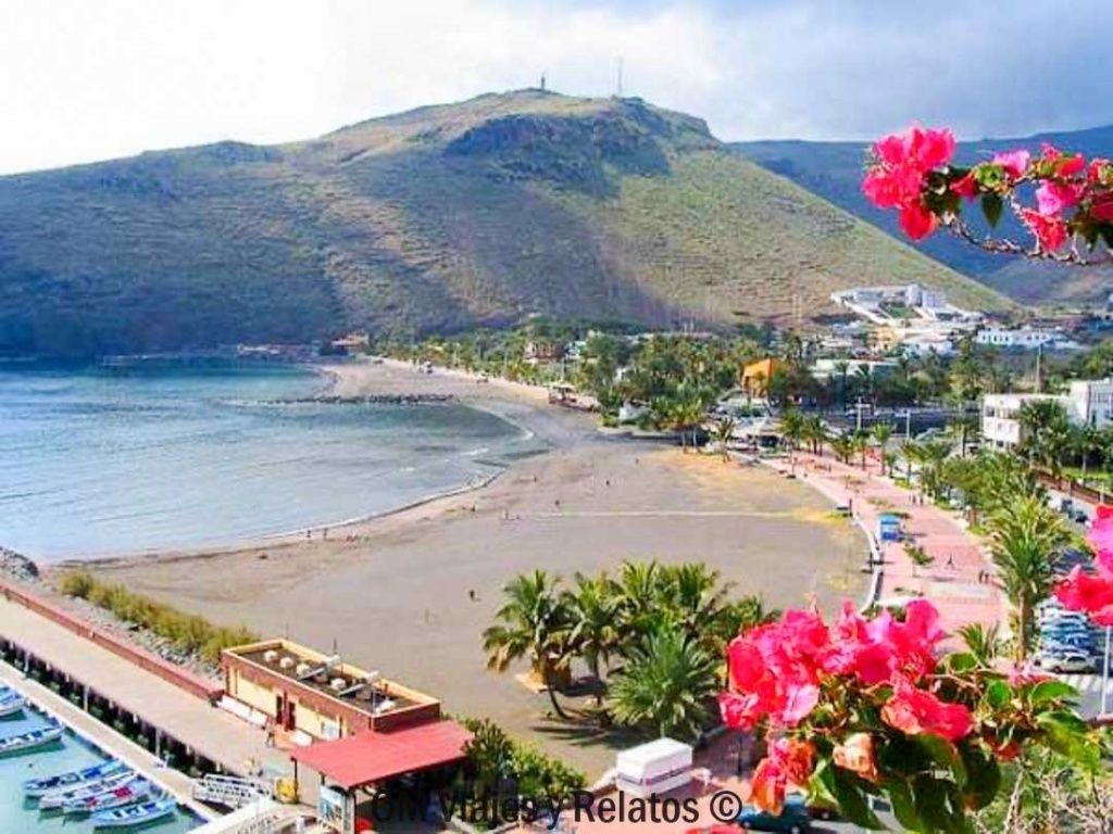 Playa de San Sebastián en La Gomera con paseo marítimo, palmeras y montañas volcánicas al fondo, una de las mejores playas de las Islas Canarias para combinar naturaleza y ambiente urbano.