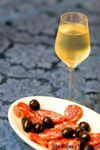Copa de vino blanco con aperitivo de embutido y aceitunas, plan gastronómico en una ruta por Cerdeña.