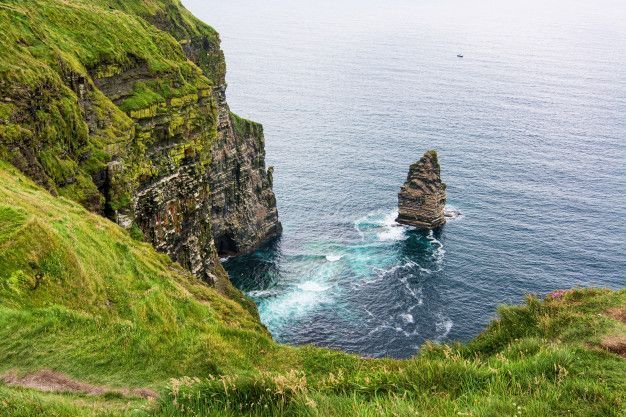 Formación rocosa junto al océano Atlántico al visitar los acantilados de Moher, rodeada de verdes paisajes irlandeses.