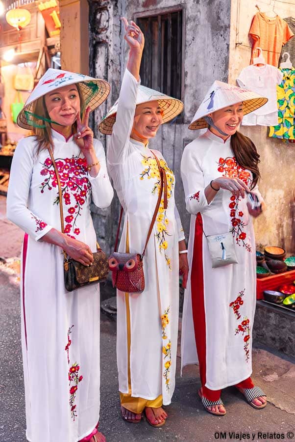 Mujeres vietnamitas con áo dài y sombreros cónicos paseando por el casco antiguo, una escena típica de que ver en Hoi An y alrededores.