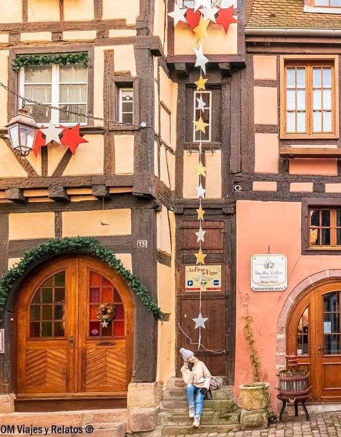Foto mía en la fachada de casa típica de Alsacia con entramado de madera y decoración en la calle, parada ideal en una ruta por los pueblos de Alsacia en coche.