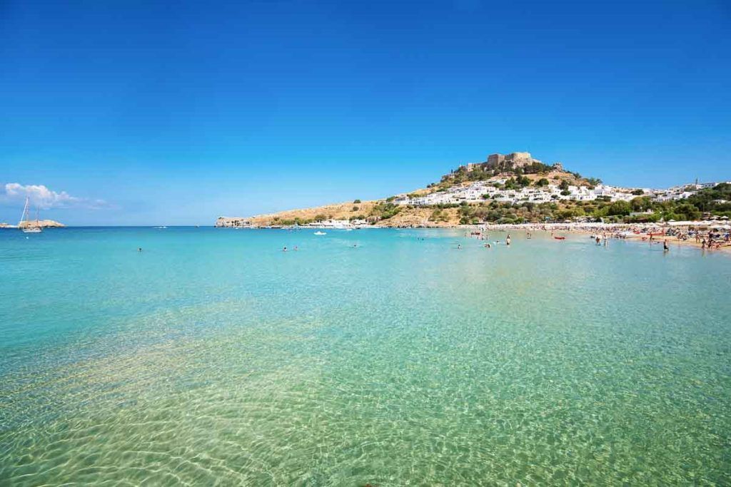 Playa de Lindos en Rodas con aguas cristalinas y la acrópolis al fondo, una parada imprescindible entre las islas griegas mas bonitas para visitar.