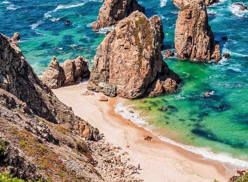 Playa salvaje de Sintra con grandes formaciones rocosas y aguas turquesas, uno de los paisajes más impresionantes que ver en Sintra en un día.
