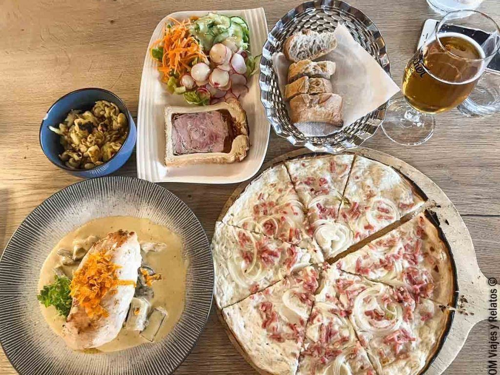 Mesa con platos típicos alsacianos, flammekueche, pescado en salsa, paté, ensalada y cerveza, una opción completa si buscas donde comer en Colmar.