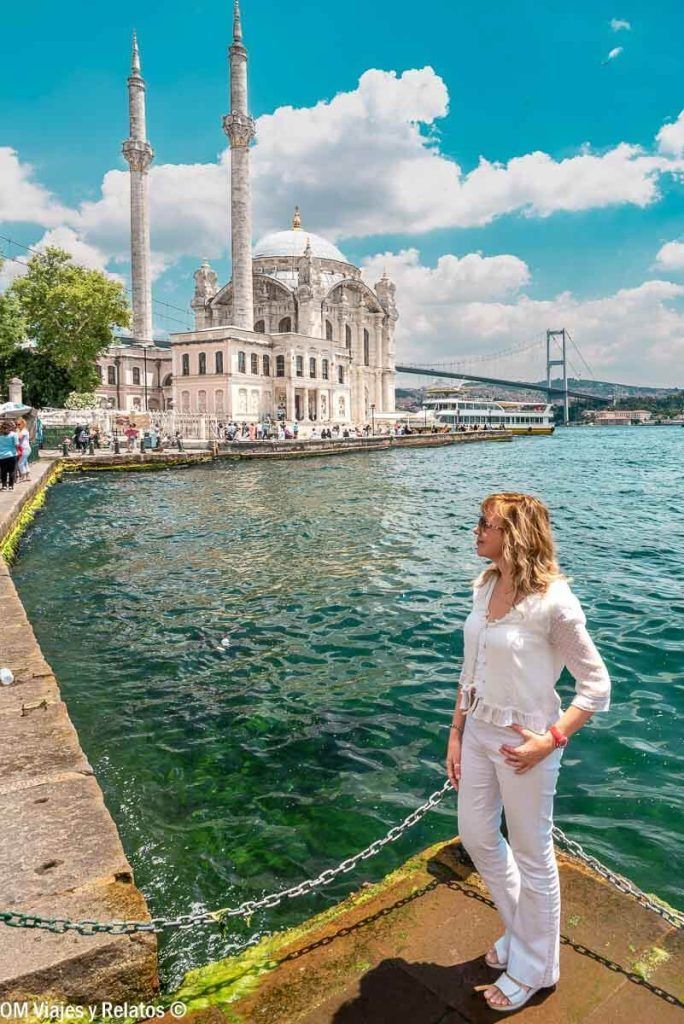 Foto mía junto al Bósforo en Ortaköy, uno de los mejores barrios donde alojarse en Estambul, con la mezquita y el puente al fondo.
