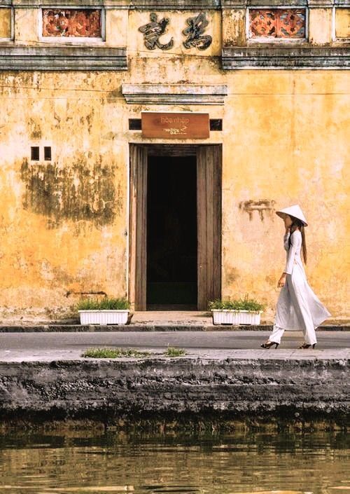 Casco histórico de Hoi An al atardecer, con mujer vestida con áo dài y sombrero vietnamita junto al río; un imprescindible de Vietnam para viajeros.