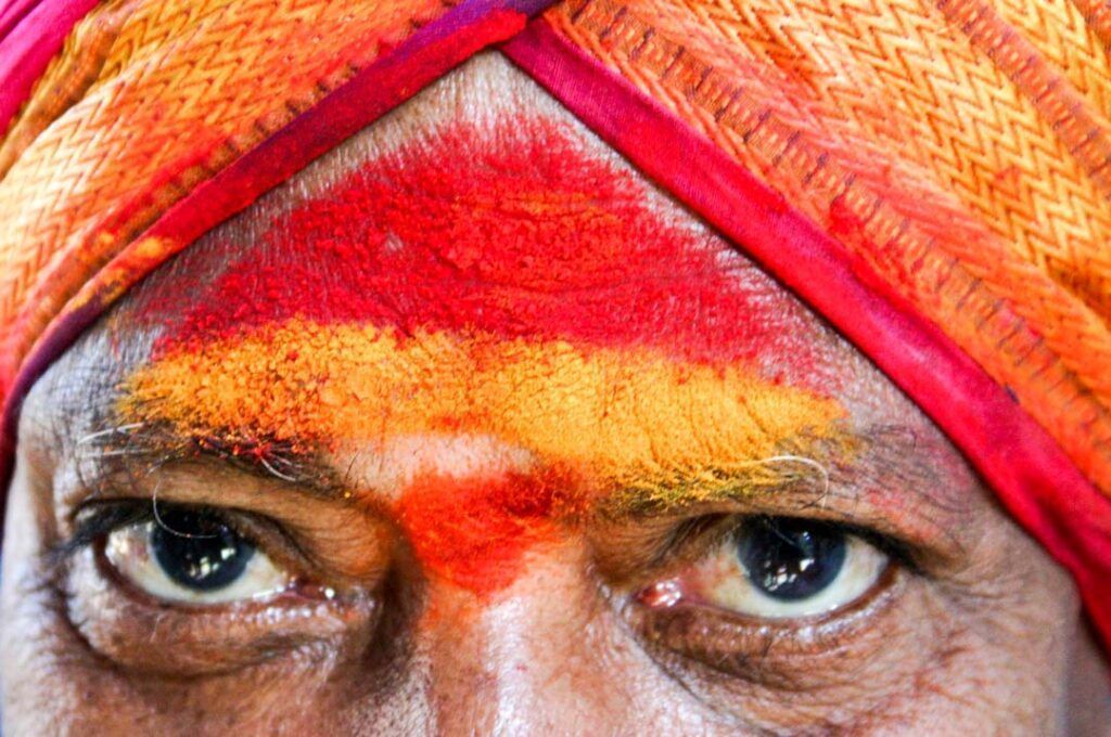 Primer plano de un hombre con turbante y rostro pintado con colores tradicionales, una imagen cultural para ilustrar consejos para viajar a la India.