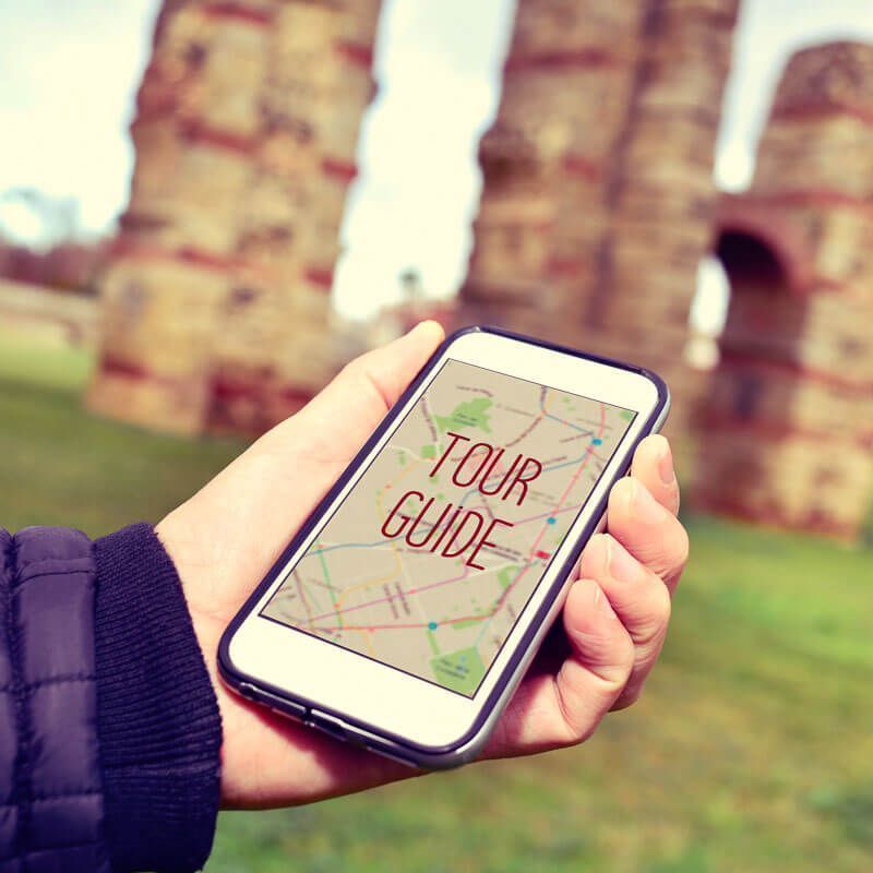 Mano sosteniendo un móvil con mapa y “Tour Guide” frente a un monumento, ideal para orientarse y usar Internet en Europa durante el viaje.