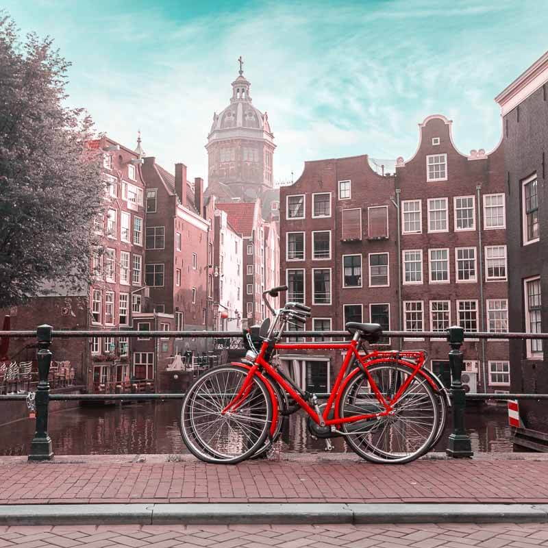 Bicicleta roja junto a un canal con casas típicas de Ámsterdam al fondo, perfecta para hablar de moverse y usar Internet en Europa con mapas y transporte.