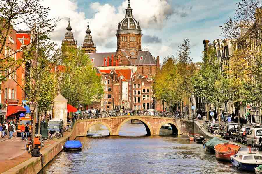 Canal con puente y la Basílica de San Nicolás al fondo, una imagen imprescindible sobre Amsterdam en un día.