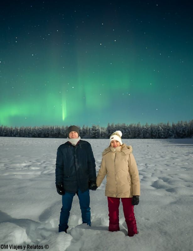 Foto en pareja de OM Viajes y Relatos sobre la nieve con la aurora boreal y cielo estrellado, ideal para ver auroras boreales en Rovaniemi.