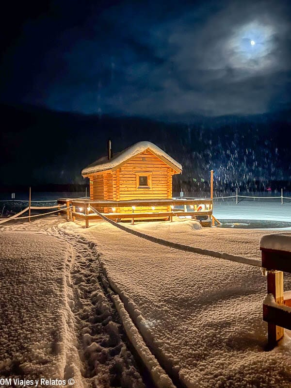 Sendero en la nieve hacia una caseta ártica bajo la luna al viajar a Laponia por libre