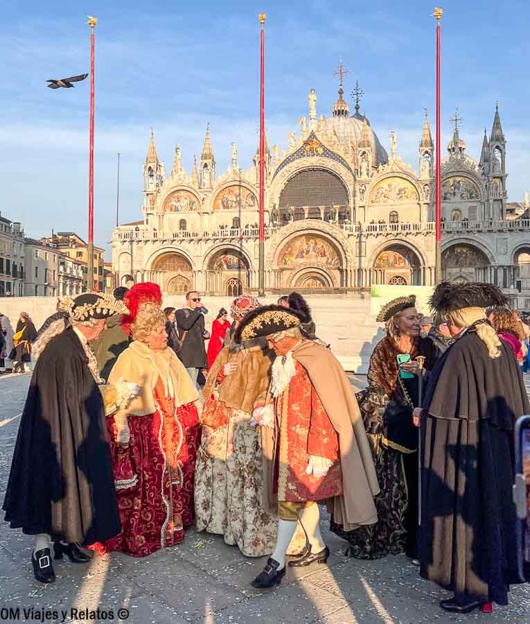 Grupo de personas con trajes de época durante el Carnaval frente a la Basílica de San Marcos, una experiencia cultural única que visitar en la Plaza de San Marcos en Venecia.