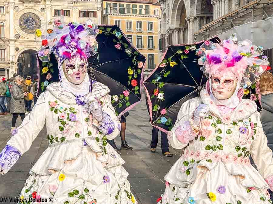 Dos personas con máscaras y paraguas decorados en la Plaza de San Marcos, una escena perfecta que hacer en Venecia en Carnaval.