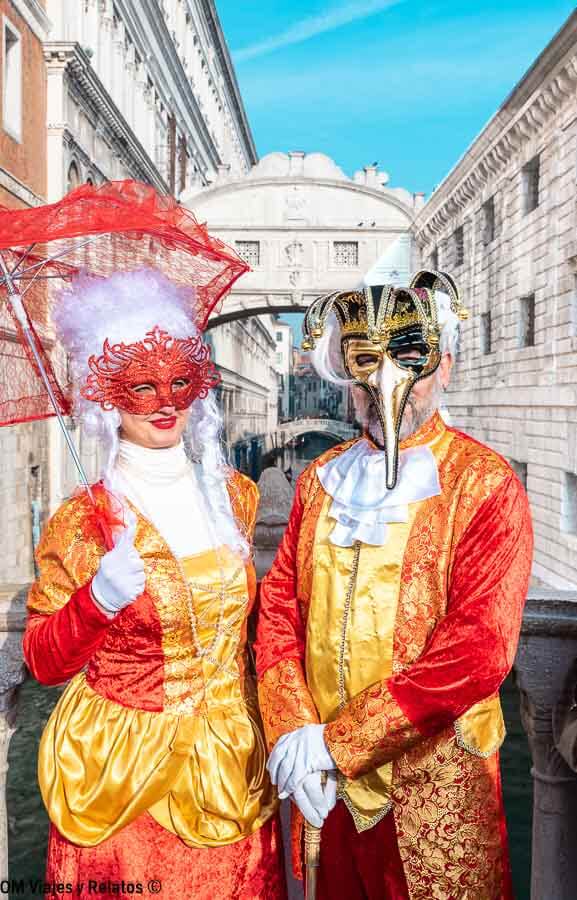 Pareja con trajes y máscaras del Carnaval posando frente al Puente de los Suspiros, un imprescindible que hacer en Venecia en Carnaval.