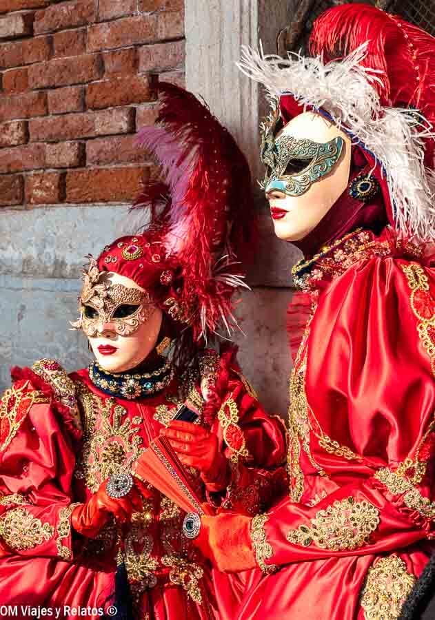 Dos personas con trajes rojos y máscaras venecianas con plumas, una de las mejores fotos que hacer en Venecia en Carnaval.