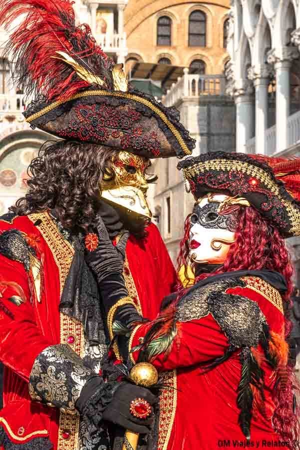 Pareja con máscaras y trajes rojos de época posando en el Carnaval de Venecia, una escena romántica que hacer en Venecia en Carnaval.