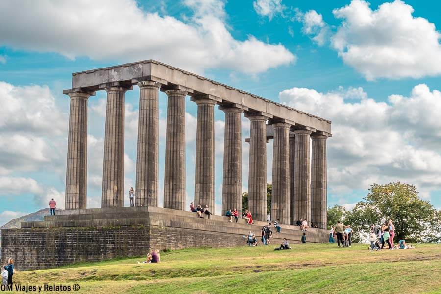 Monumento Nacional de Escocia en Calton Hill con visitantes descansando en el césped, un sitio histórico que ver en Edimburgo en 4 días.