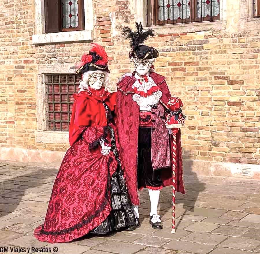 Pareja con trajes rojos y máscaras barrocas posando en Venecia, una de las escenas más típicas que hacer en Venecia en Carnaval.