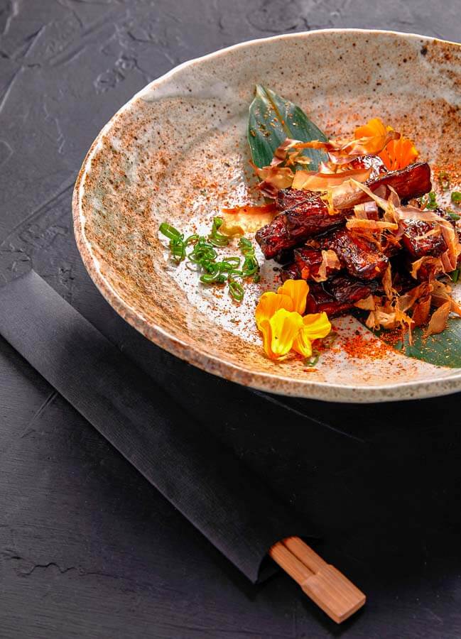 Plato de cocina japonesa gourmet con carne glaseada y flores comestibles, consejos para viajar a Japón por libre: probar menús degustación y reservar restaurantes populares.