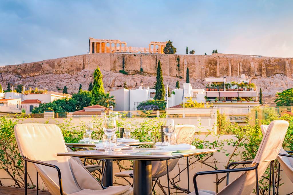 Terraza con mesa lista para cenar y vistas a la Acrópolis al atardecer, un plus brutal al elegir donde alojarse en Atenas.