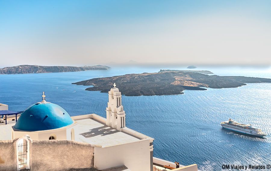 Vista de Fira con cúpula azul y la caldera de Santorini al fondo, una imagen ideal para hablar de donde alojarse en Santorini.