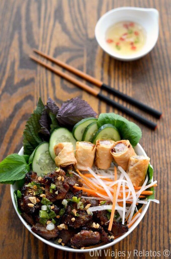 Plato vietnamita con rollitos, hierbas frescas y salsa en mesa con palillos, consejos para viajar a Vietnam por libre.