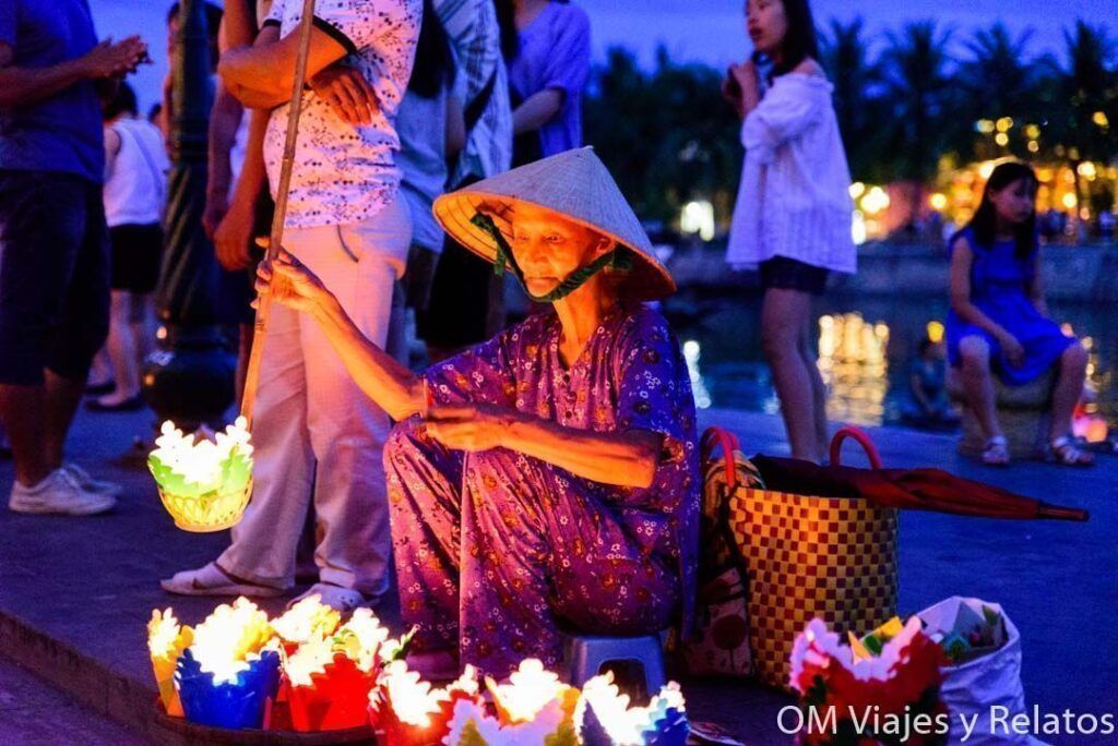 Mujer con sombrero cónico vendiendo farolillos de papel encendidos en Hoi An durante el festival de luna llena, una escena imprescindible en consejos para viajar a vietnam por libre.