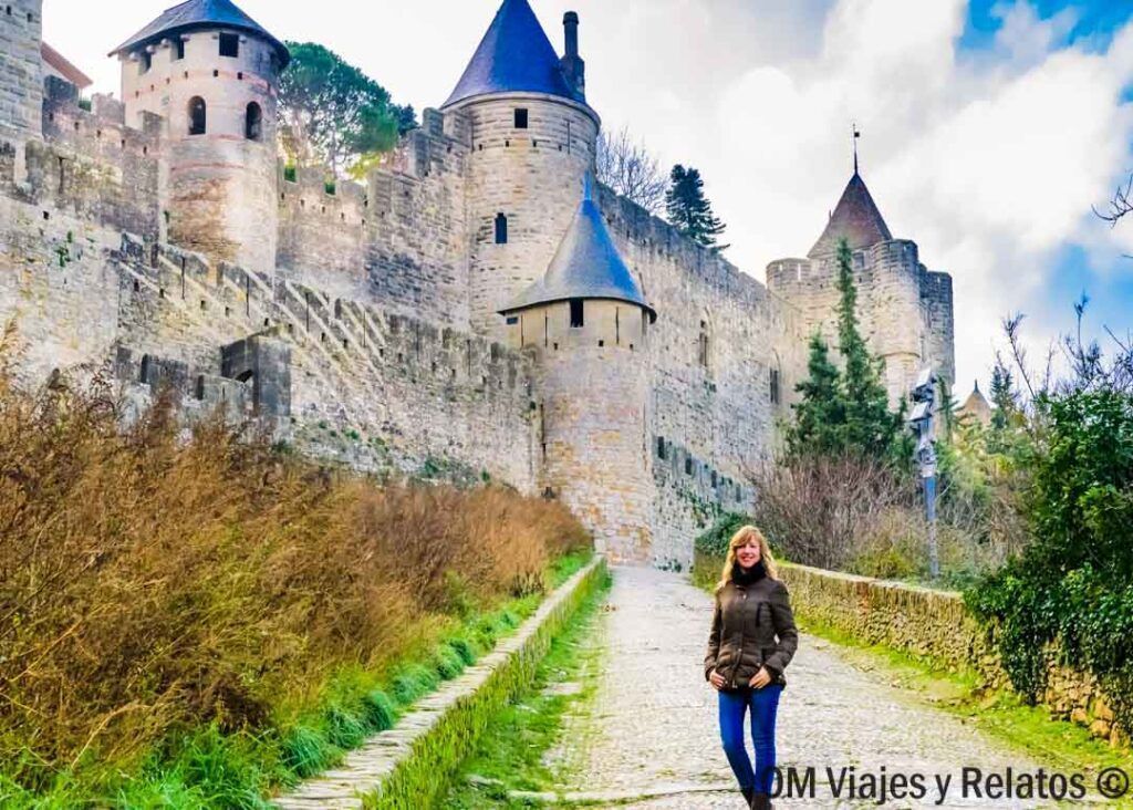 Foto mía paseando junto a las murallas medievales de la ciudad fortificada de Carcasona, una parada imprescindible en una ruta por Occitania.