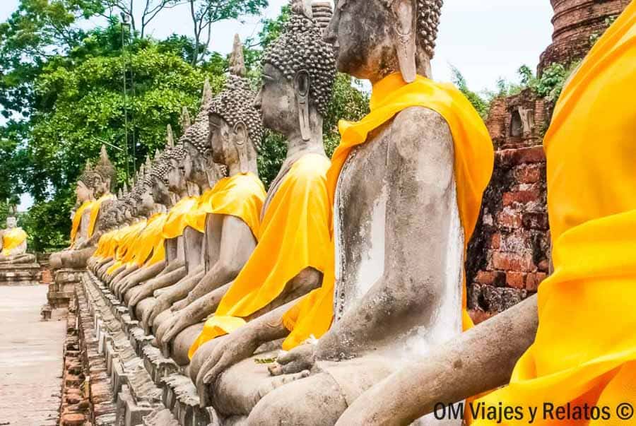 Budas sentados alineados con manto naranja en un templo histórico de Ayutthaya en un día de viaje por Tailandia
