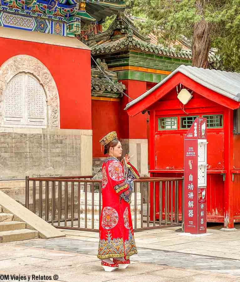 Mujer con traje tradicional chino frente a edificios rojos en un templo de Pekín, escena típica de que ver en Pekín en 4 días.