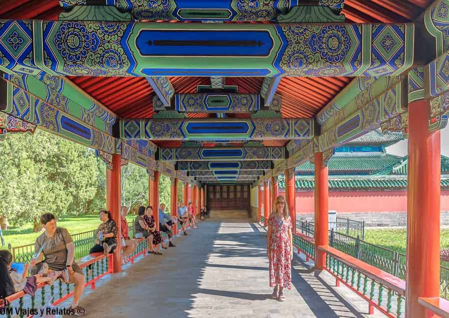 Foto mía caminando por la galería cubierta con columnas rojas y techos decorados, una escena imprescindible al visitar el Templo del Cielo de Pekín.