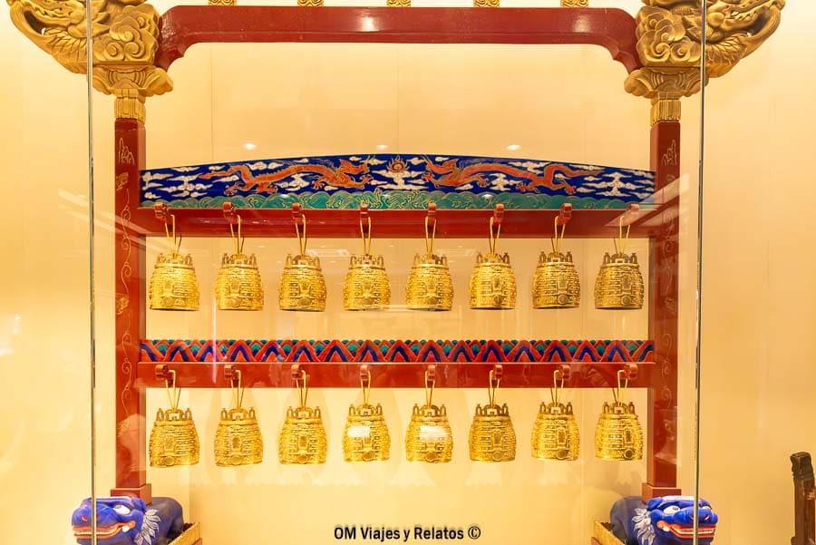 Visitar el Templo del Cielo de Pekín: campanas rituales doradas en vitrina con detalles ornamentales tradicionales.