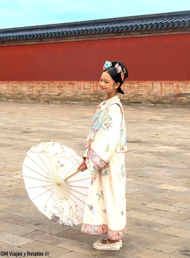 Mujer con traje tradicional chino y sombrilla en el recinto, una escena cultural al visitar el Templo del Cielo de Pekín.
