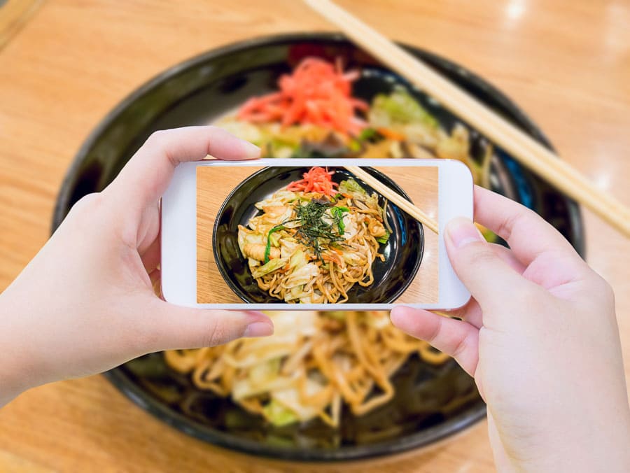Mis manos fotografiando un bol de fideos japoneses con el móvil, consejos para viajar a Japón por libre: probar la comida local y usar traductor de menús.