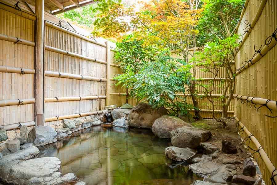 Onsen privado rodeado de bambú y rocas en un jardín japonés, experiencia auténtica de aguas termales en Japón.