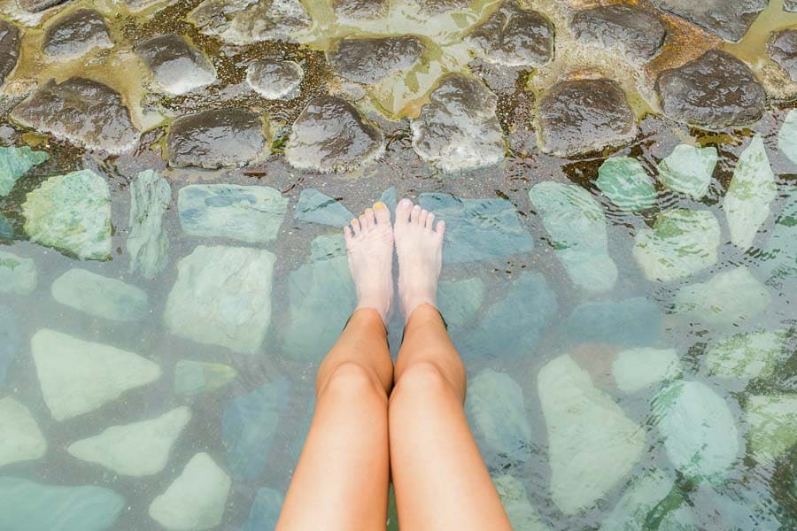 Mis piernas y pies relajándose en un baño al aire libre con piedras, experiencia de aguas termales en Japón.