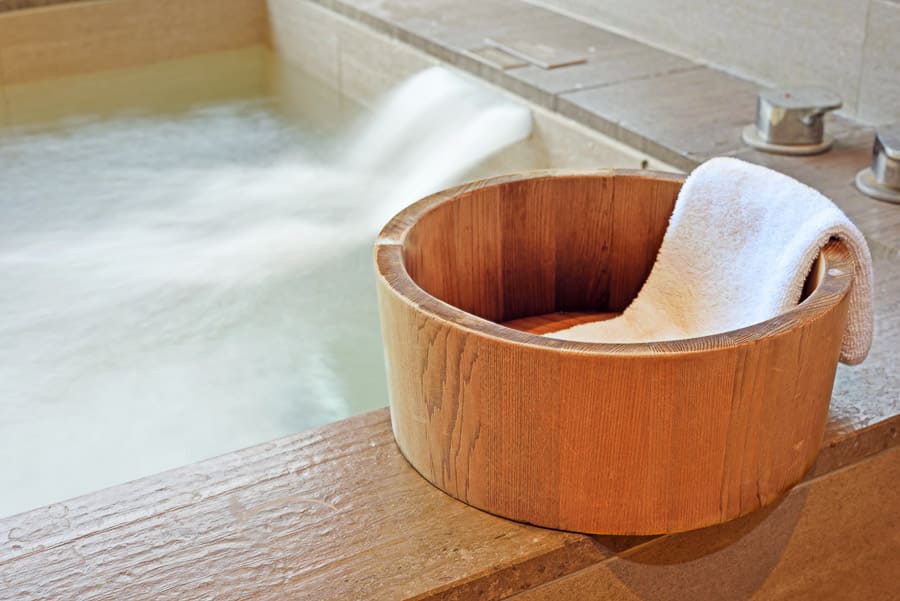 Ofuro de madera con toalla junto a una bañera de agua caliente, ritual de relax en aguas termales en Japón.