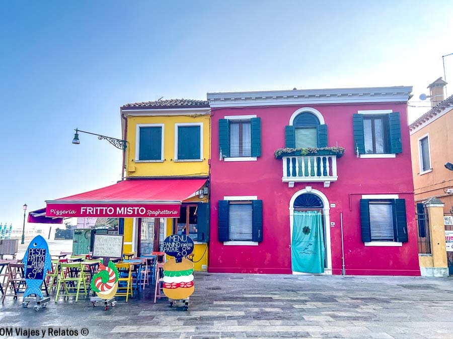Casas de colores en Burano con terraza de restaurante y carteles de comida, una parada imprescindible en que ver en Burano.