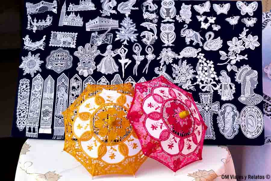 Muestras de encaje de Burano con sombrillas decorativas y dibujos artesanales, un imprescindible en que ver en Burano.