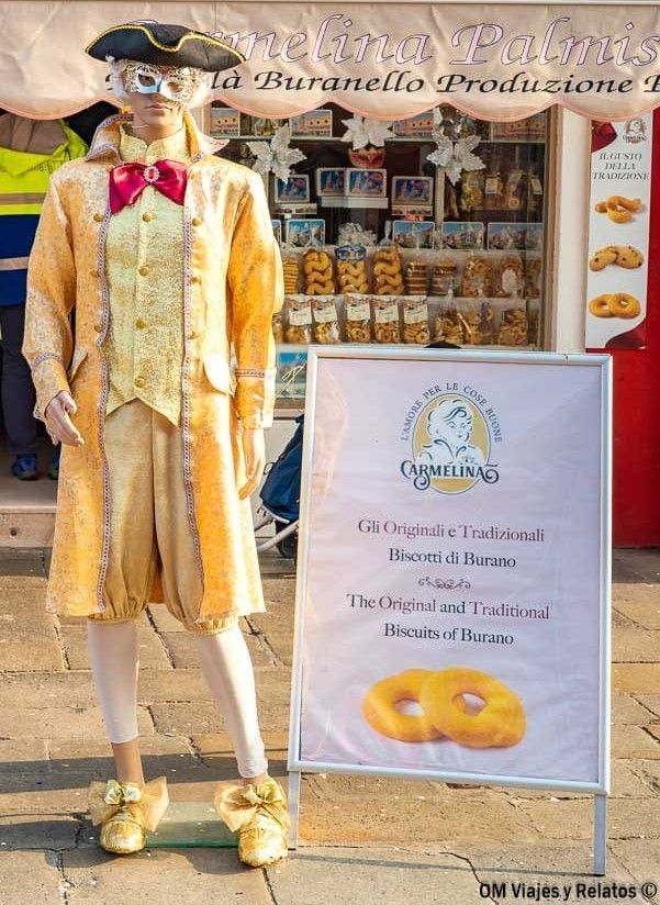 Figura con disfraz veneciano frente a tienda de galletas típicas de Burano, una parada curiosa en que ver en Burano.