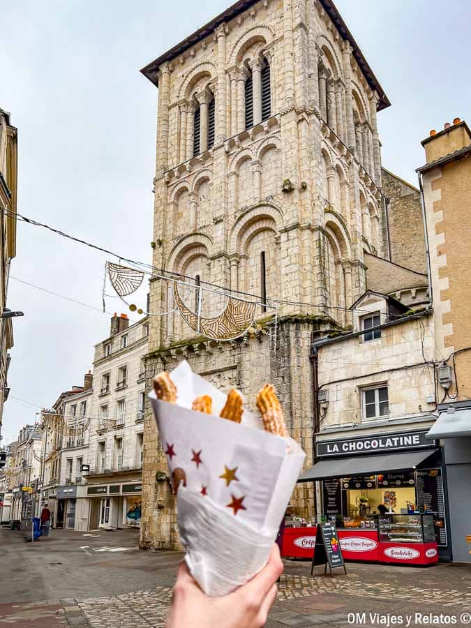 Churros en primer plano con una torre de iglesia en Poitiers al fondo, un plan foodie durante una ruta por Aquitania.