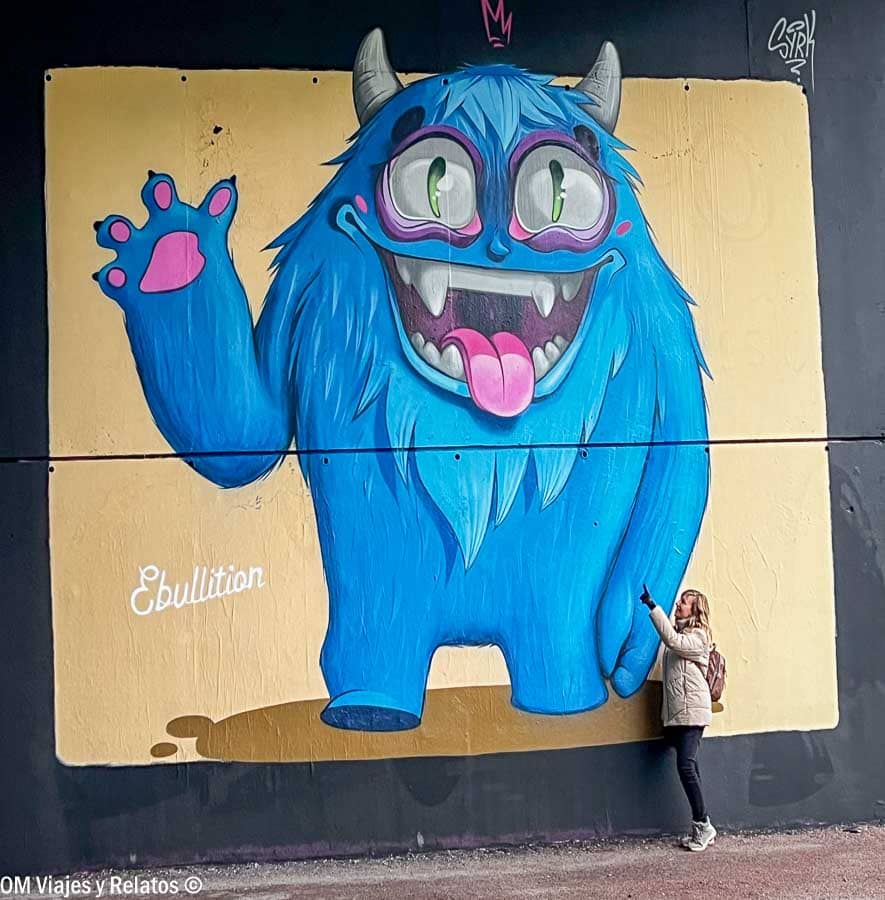 Servidora posando junto a un mural de arte urbano con un monstruo azul en Poitiers, una parada divertida en una ruta por Aquitania.