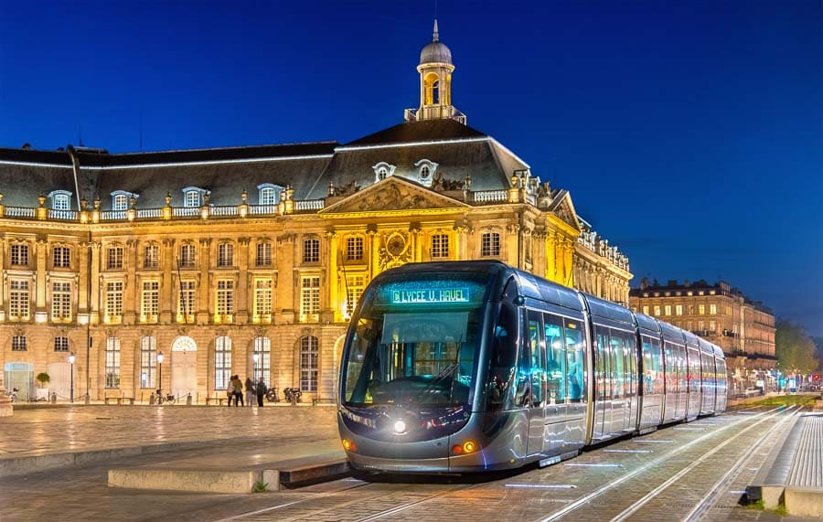 Tranvía en Burdeos de noche pasando por la Place de la Bourse iluminada, un plan urbano imprescindible en una ruta por Aquitania.